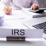 IRS Nameplate In Front Of Accountant Calculating Tax
