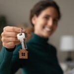 Close up focus on keys, smiling woman realtor selling apartment